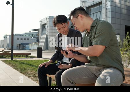 Deux jeunes Chinois regardent des vidéos en ligne sur smartphone d'homme d'affaires en milieu urbain Banque D'Images