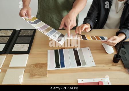 Les mains de deux jeunes créateurs discutent d'échantillons textiles tout en pointant l'un d'eux par lieu de travail Banque D'Images