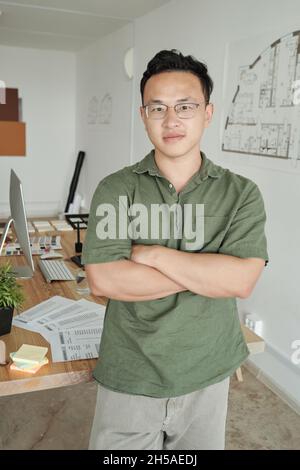 Jeune homme confient designer croisant les bras par la poitrine tout en se tenant devant la caméra contre son lieu de travail Banque D'Images