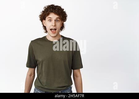 Image de jeune homme regardant surpris et étonné à la caméra, coeur quelque chose d'intéressant, debout sur fond blanc Banque D'Images