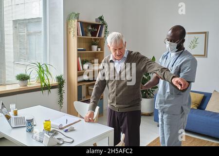 Médecin africain en masque examinant son patient senior pendant l'examen médical à l'hôpital Banque D'Images