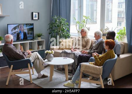 Groupe de personnes âgées se reposant sur un canapé dans le salon et regardant les nouvelles à la télévision ensemble Banque D'Images