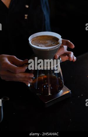 le barista verse de l'eau chaude sur du café à bulles brunes rugueuses par le filtre goutte-à-goutte. préparation du café à l'aide de chemex. versez sur la cafetière a. Banque D'Images