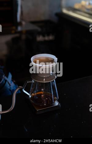 le barista verse de l'eau chaude sur du café à bulles brunes rugueuses par le filtre goutte-à-goutte. préparation du café à l'aide de chemex. versez sur la cafetière a. Banque D'Images