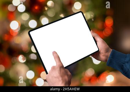 Tablette dans les mains avec les lumières de l'arbre de Noël derrière.Affichage isolé pour la promotion de la conception.Concept d'achat en ligne de saison Banque D'Images