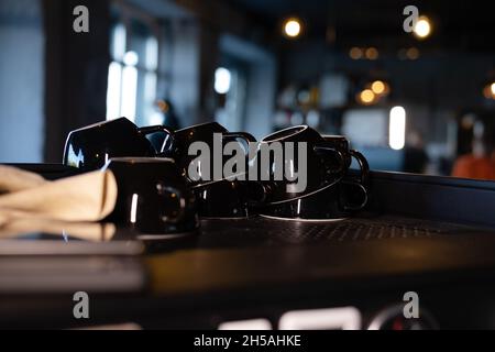 Pile de tasses à café noires vides sur l'étagère ou la machine à café dans le café à l'intérieur. Banque D'Images