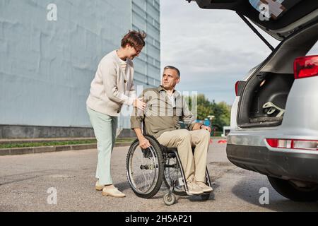 Portrait complet d'un couple d'âge mûr avec un homme en fauteuil roulant laissant le stationnement à l'extérieur, espace de copie Banque D'Images