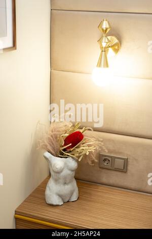 Vase en pierre moderne silhouette féminine avec fleurs séchées sur la table de chevet dans la chambre.Mise au point sélective et douce, bruit artistique Banque D'Images