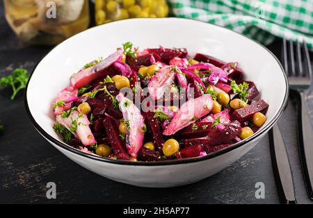 Salade de hareng, pois verts et betteraves remplies d'huile végétale sur une table sombre. Banque D'Images