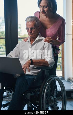 Femme regardant l'ordinateur portable d'un fauteuil roulant derrière son épaule Banque D'Images