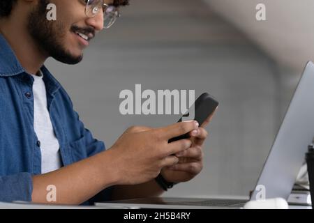 Gros plan Happy Casual Indian man utilisant un smartphone et un ordinateur portable dans le café Banque D'Images