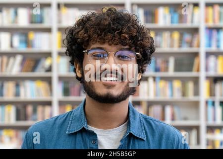 Portrait d'un jeune étudiant indien souriant à l'arrière-plan, à la bibliothèque Banque D'Images