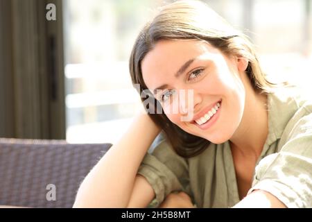 Une femme heureuse avec un sourire blanc parfait vous regarde assis dans un bar Banque D'Images