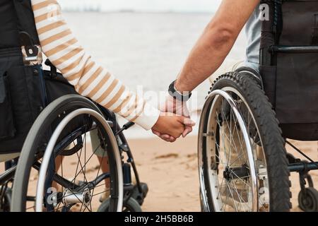 Gros plan d'un couple aimant en fauteuil roulant tenant les mains sur la plage au bord de l'océan, espace de copie Banque D'Images