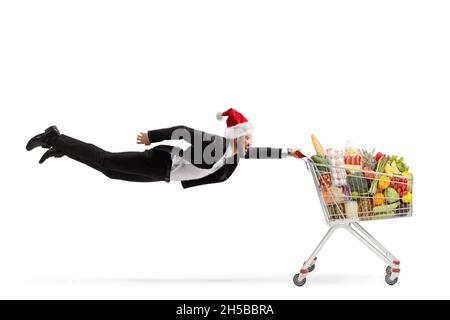 Photo en longueur d'un homme d'affaires avec un chapeau de noël du père noël volant et tenant un panier avec nourriture isolée sur fond blanc Banque D'Images