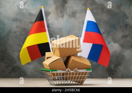 Boîtes en carton dans un panier et deux drapeaux sur un fond abstrait, le concept de commerce entre l'Allemagne et la Russie Banque D'Images