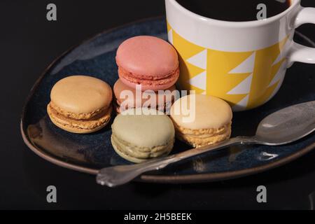 Macarons avec une tasse de café sur fond noir. Banque D'Images