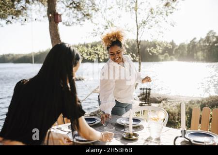 Une femme souriante établit une table avec une amie pendant le dîner le jour ensoleillé Banque D'Images