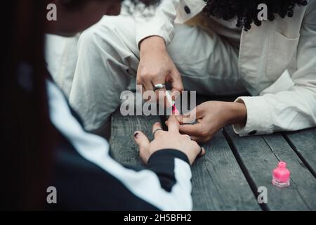 Section médiane du garçon peignant les ongles de l'ami mâle avec du vernis rose à la table Banque D'Images