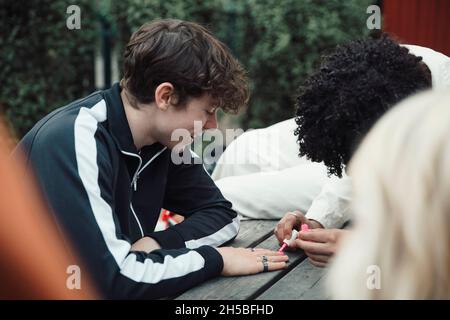 Garçon adolescent souriant regardant un ami mâle appliquant du vernis à ongles rose Banque D'Images