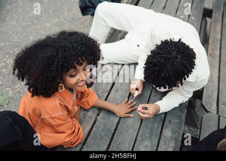 Vue en grand angle de l'adolescent de sexe masculin appliquant du vernis à ongles à une amie de sexe féminin assise sur une table Banque D'Images