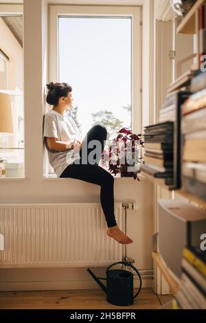 Jeune femme assise dans la fenêtre à la maison Banque D'Images