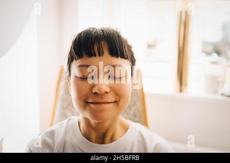 Jeune femme souriante avec les yeux fermés à la maison Banque D'Images