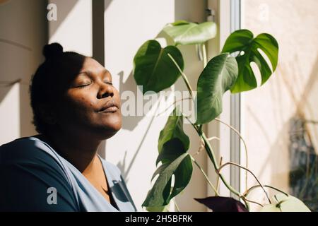 Femme adulte de taille moyenne debout avec les yeux fermés au soleil à la maison Banque D'Images