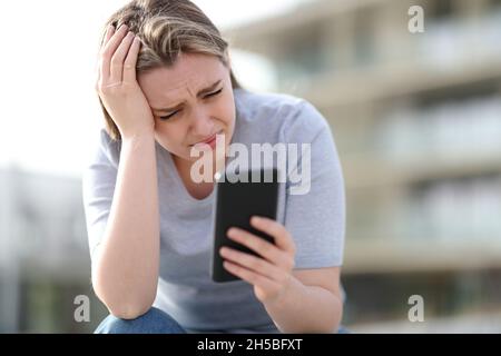 Triste adolescent se plaint de vérifier le contenu de smartphone assis dans la rue Banque D'Images