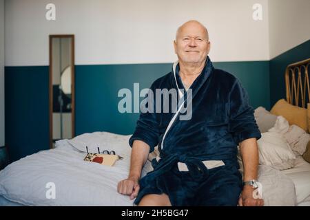 Portrait d'un homme âgé souriant en peignoir sur le lit à la maison Banque D'Images