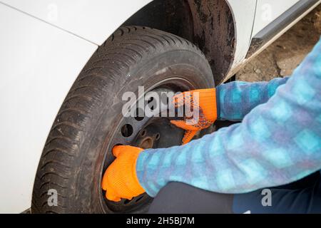 Remplacement d'un pneu crevé endommagé.Mains auto mécanicien tenant un pneu sale sur la voiture.attention sélective sur les mains Banque D'Images