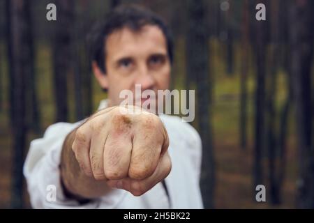 Homme de karaté dans un vieux kimono et ceinture noire punch d'entraînement à la forêt.Concept des arts martiaux.Pins à l'arrière-plan. Banque D'Images