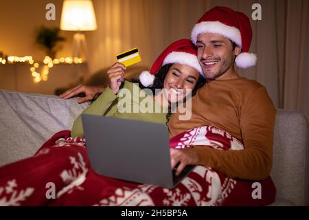 Couple faisant des achats de Noël en utilisant un ordinateur portable et une carte de crédit à l'intérieur