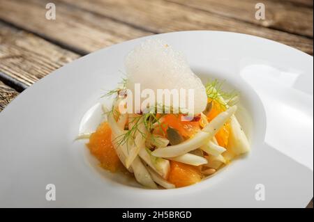 Salade gastronomique de fenouil cru et d'oranges avec mousse parfumée, gros plan sur une assiette blanche sur une table en bois Banque D'Images