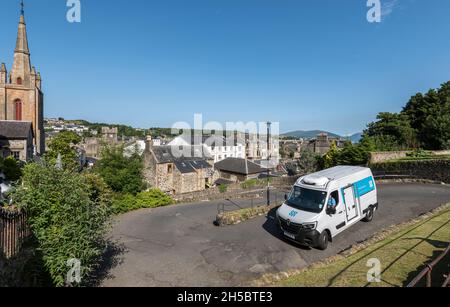 Camion de livraison négociant des virages en épingle à cheveux près du fond de la route de Serpentine, Rothesay; église, horizon de la ville et collines lointaines en arrière-plan. Banque D'Images