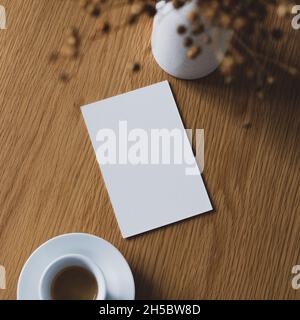 Carte d'invitation vierge maquette, tasse de café et vase de lin séché sur table en bois dans le café Banque D'Images