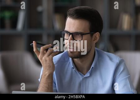 Jeune homme d'affaires concentré enregistrant des messages audio sur un téléphone portable. Banque D'Images