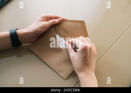 Vue rapprochée en grand angle d'une jeune femme méconnue tenant dans une enveloppe de mains avec lettre reçue assise à une table. Banque D'Images