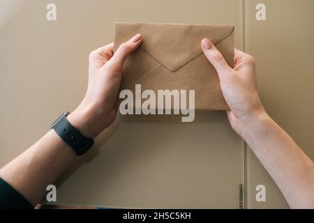 Vue rapprochée en grand angle d'une jeune femme méconnue tenant dans une enveloppe de mains avec lettre reçue assise à une table. Banque D'Images