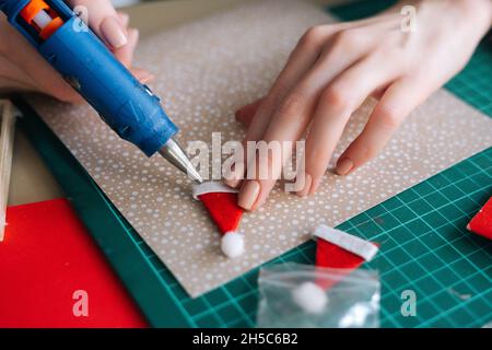 Gros plan des mains de jeune femme méconnaissable encollant des enveloppes à bord avec des cadeaux pour les enfants faisant le calendrier de l'Avent de Noël à la maison. Banque D'Images