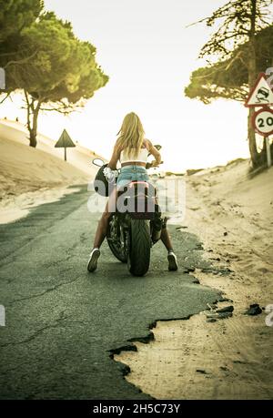 Vue arrière d'une femme sur une moto dans les dunes de sable au coucher du soleil, Tarifa, Cadix, Andalousie, Espagne Banque D'Images