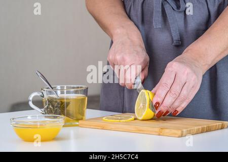 L'hôtesse prépare du thé vitaminé, coupe une tranche de citron.Le thé au citron et au miel stimulera l'immunité en cas de pandémie.Protection contre le coronavirus Banque D'Images