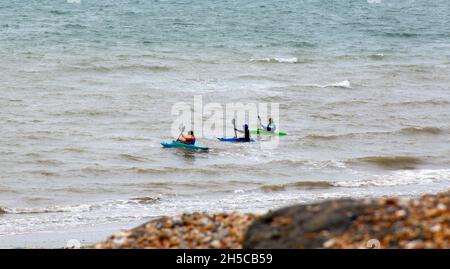 Trois personnes dans des kayaks paddeling près de la rive de Bulverhythe, Sussex, Angleterre, Royaume-Uni. Banque D'Images