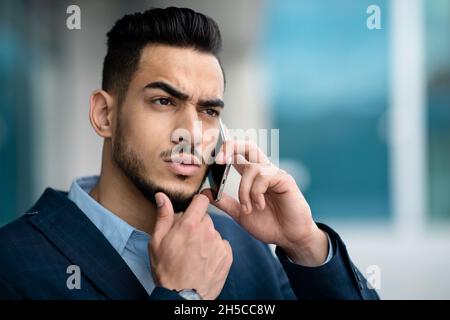 Homme d'affaires du Moyen-Orient confus ayant une conversation téléphonique, portrait de gros plan, panorama Banque D'Images