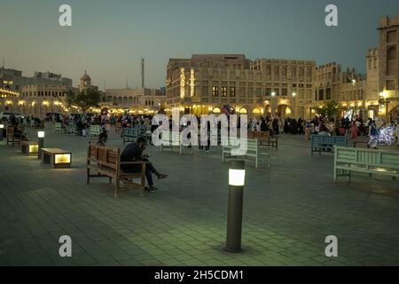 Souq Waqif à Doha, Qatar rue principale au coucher du soleil montrant la traditionnelle arabe magasin de textile, cafés, locaux et les visiteurs marchant. Banque D'Images