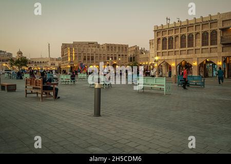 Souq Waqif à Doha, Qatar rue principale au coucher du soleil montrant la traditionnelle arabe magasin de textile, cafés, locaux et les visiteurs marchant. Banque D'Images