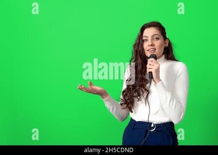 haut-parleur de conférence féminin pendant la présentation, tient le microphone et fait quelques gestes, isolés sur le vert Banque D'Images