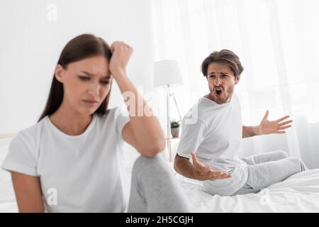 Agressif mal millénaire mari caucasien avec des cris de chaume et des essaims à offensé triste femme déprimée dans la chambre à coucher Banque D'Images