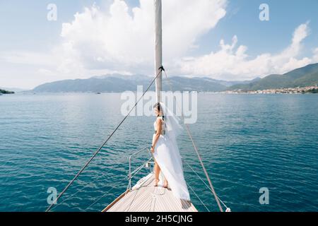 La mariée se tient sur l'arc du yacht naviguant dans la baie de Kotor, vue arrière Banque D'Images