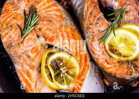 Vue de dessus des steaks de saumon rouge fraîchement torréfiés avec herbes, épices et citron sur fond d'assiette en métal noir dans la cuisine. Banque D'Images